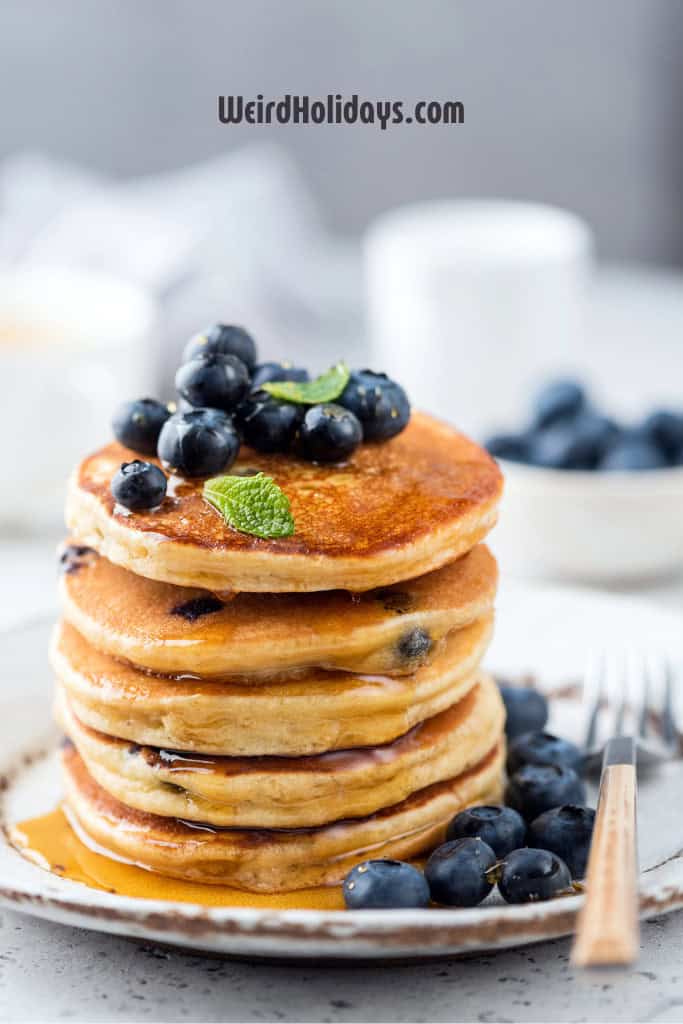 pile of blueberry pancakes on a plate topped with blueberries