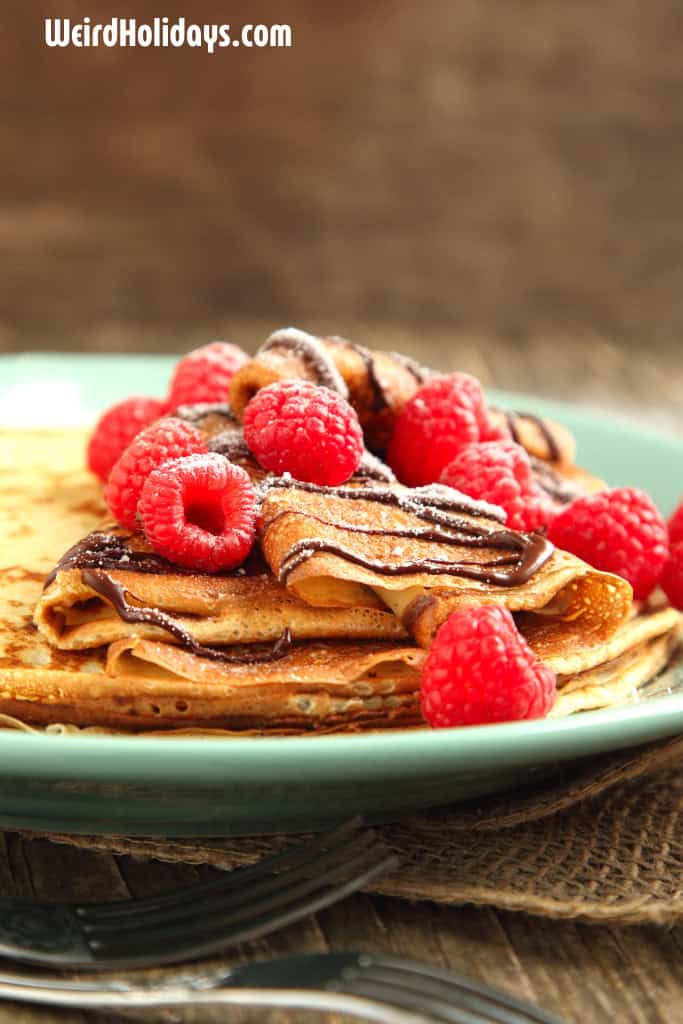 plate of crepes with raspberries and chocolate sauce