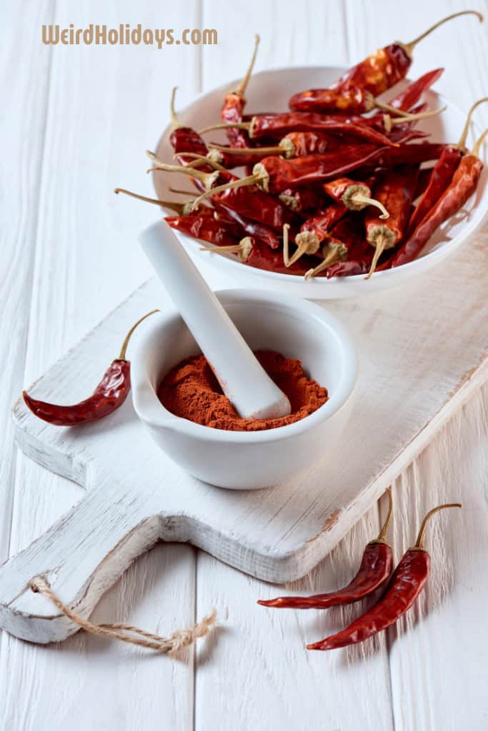 red hot chillis in a white bowl next to a pestle and morter with chili powder in