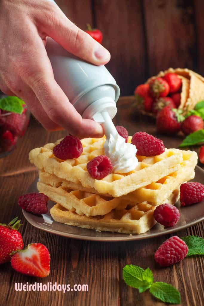 spraying whipped cream on top of waffles with raspberries