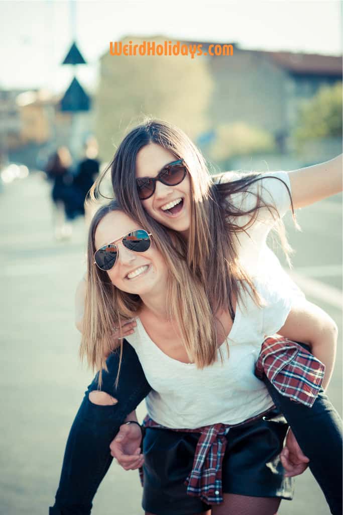 2 girlfriends smiling giving each other a piggy back.