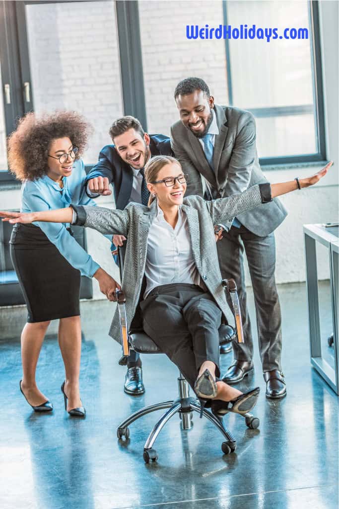 4 adults messing about at work pushing someone on a chair