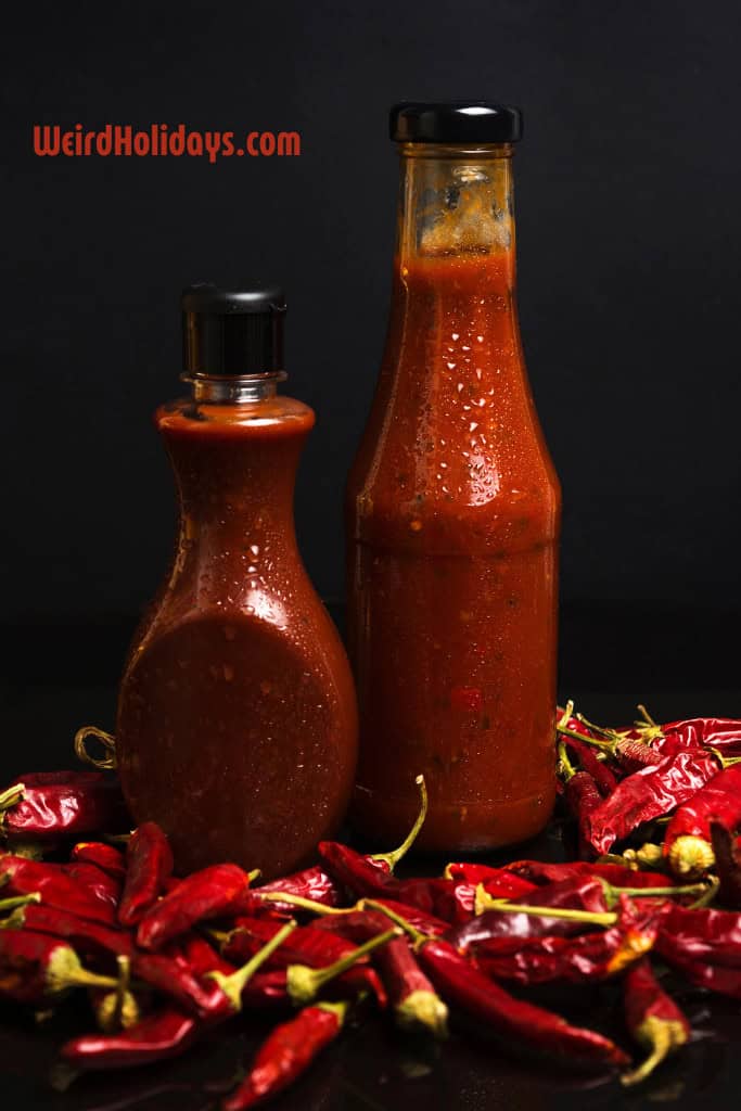 2 bottles of red hot sauce surrounded by chillis