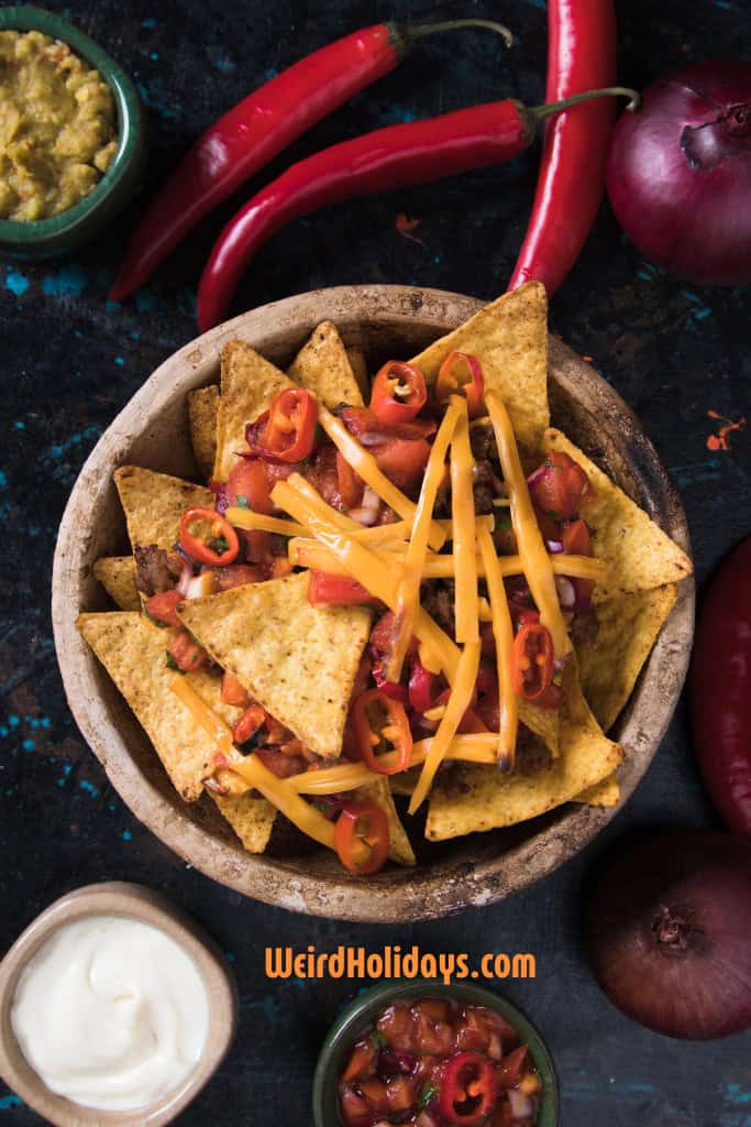 bowl of nachos with tortilla chips, chilis, cheese sauce and salsa