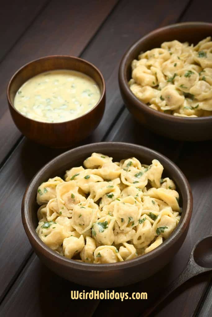 2 bowls of tortellini on a table with creamy sauce in a bowl next to it. 